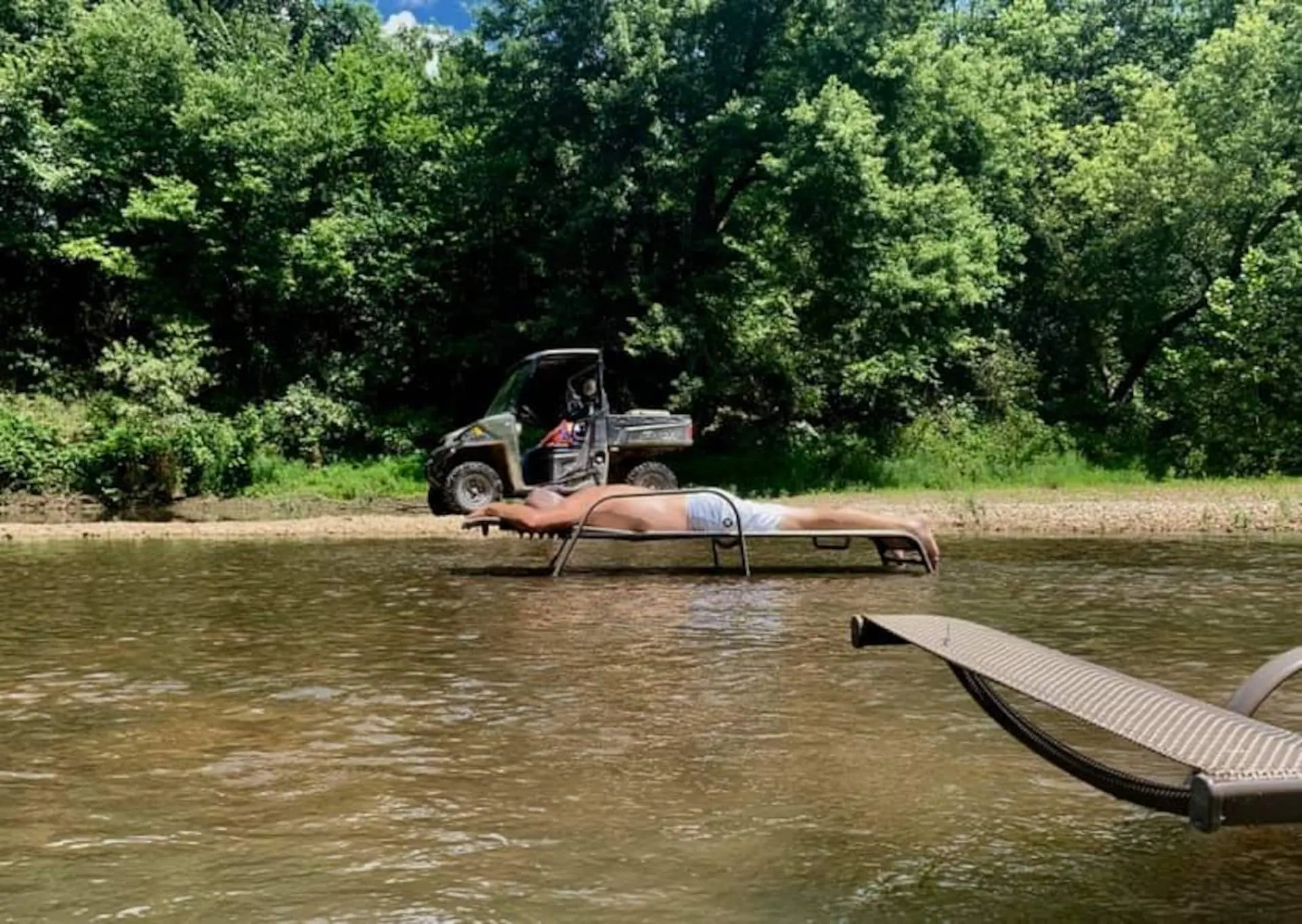 A guest stretched out on a lounger in the Sac River with the farm side-by-side parked on the bank